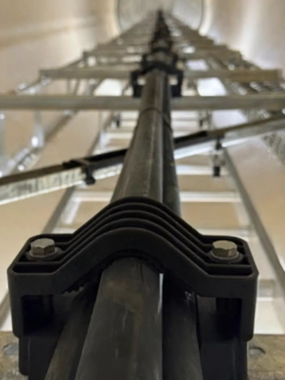 Close-up of îd-Technik cable clamps holding MV electrical cables along a vertical ladder rack within a high-voltage infrastructure environment.